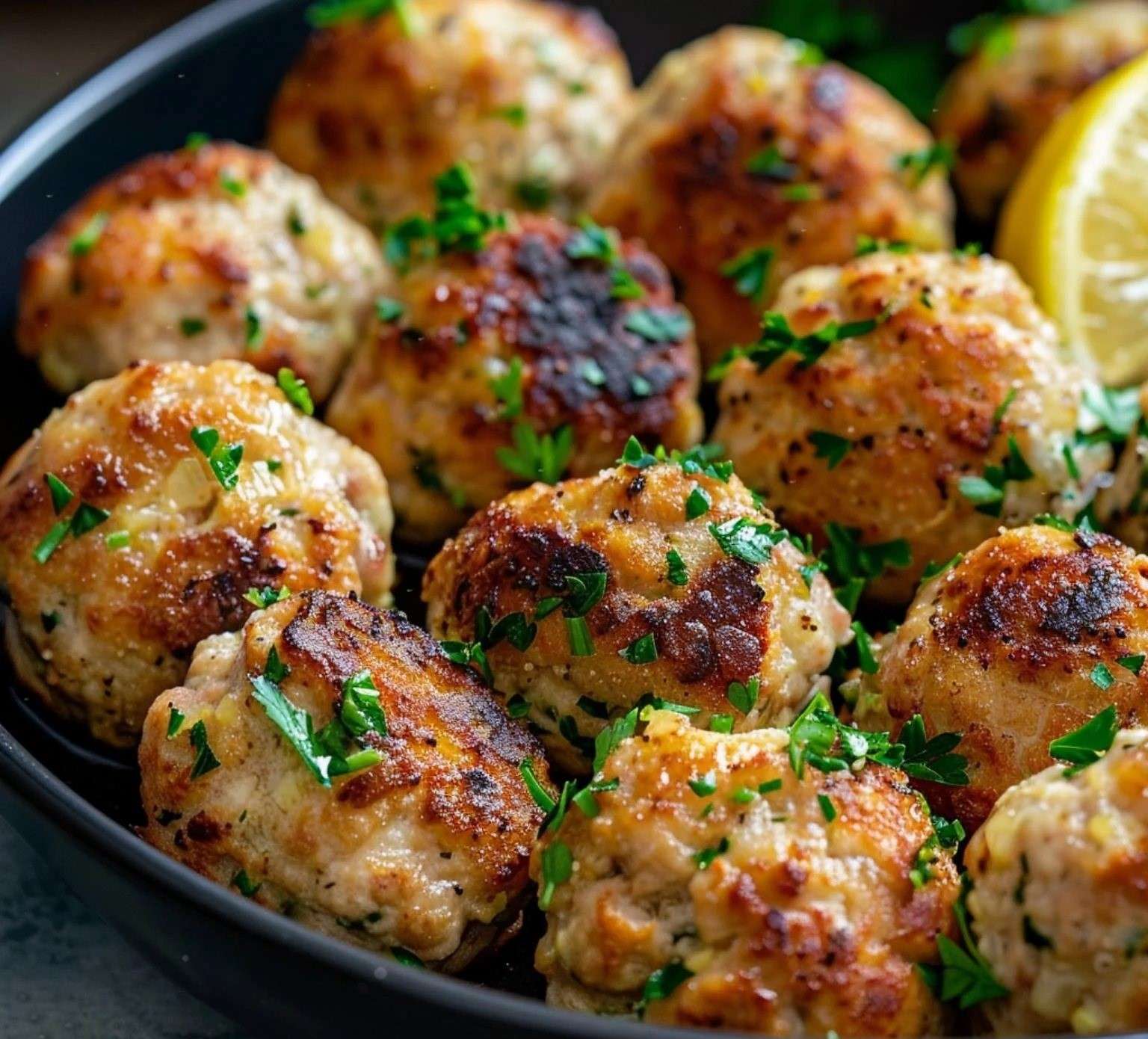 Boulettes de poulet dorées servies avec une sauce au citron crémeuse et parsemées de persil frais.