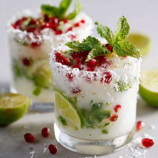 Verres de mojito coco de Noël décorés de noix de coco et grenade sur table festive.