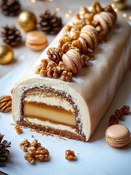 Bûche vanille caramel aux noix décorée de macarons, noix de pécan et sucre glace, présentée sur un plat de fête pour un dessert de Noël gourmand.