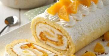 Roulé mangue mascarpone tranché, montrant une spirale de biscuit doré et de crème à la mangue, décoré de morceaux de mangue fraîche sur un plat de service.