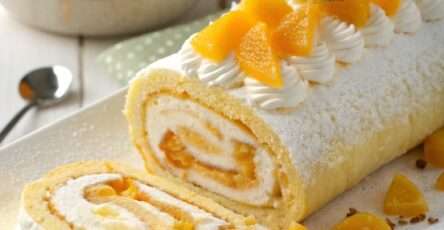 Roulé mangue mascarpone tranché, montrant une spirale de biscuit doré et de crème à la mangue, décoré de morceaux de mangue fraîche sur un plat de service.