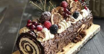 Bûche de Noël chocolat vanille décorée de fruits rouges, orange séchée et sucre glace effet forêt enchantée