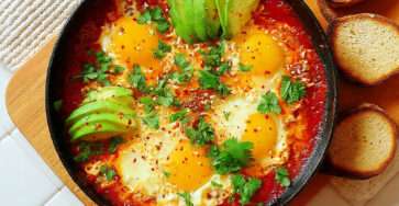 Shakshuka aux œufs et avocat avec sauce tomate, feta et herbes fraîches