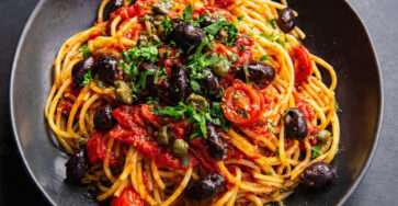 Spaghetti sauce tomate aux olives noires et câpres servis dans une assiette méditerranéenne