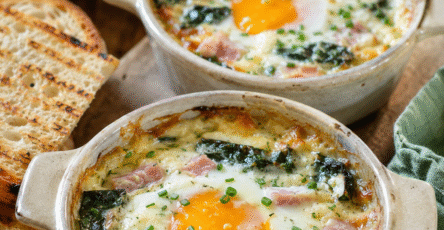 Œufs cocotte blettes, jambon blanc et tomme râpée servis dans des ramequins rustiques avec crème fondante et pain grillé.