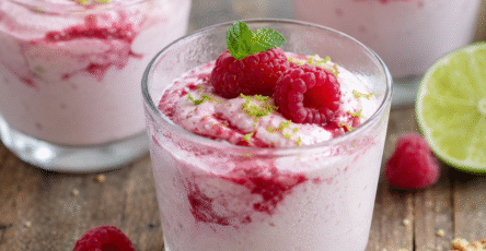 Mousse framboises yaourt grec servie en verrines avec citron vert, framboises fraîches et menthe sur une table rustique.