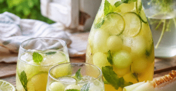 Boisson melon menthe au citron vert servie dans une carafe avec glaçons, billes de melon, rondelles de citron vert et feuilles de menthe.