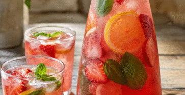 Limonade fraise basilic servie dans une carafe avec fraises fraîches, rondelles de citron, feuilles de basilic et glaçons.