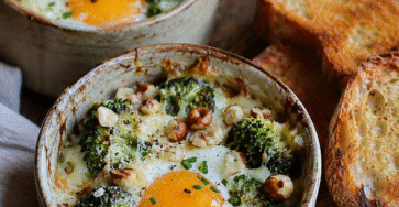 Œufs cocotte brocoli, fromage frais et noisettes servis dans des ramequins rustiques avec crème onctueuse et pain grillé.