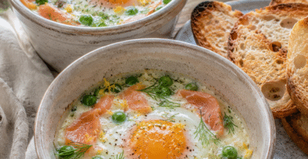 Œufs cocotte petits pois, saumon fumé et aneth servis dans des ramequins rustiques avec crème légère et pain grillé.