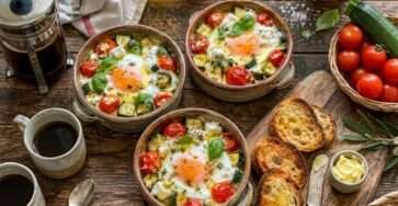 Œufs cocotte courgettes, tomates cerises et chèvre frais servis dans des ramequins rustiques avec basilic frais et pain grillé.